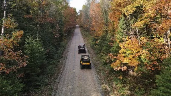 Two UTVs driving up a trail throuw the fall color trees