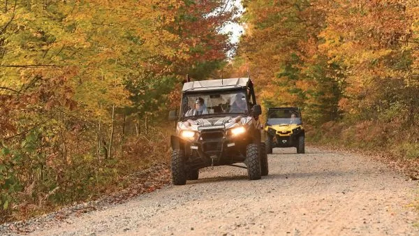 Two UTVs driving towards the camera up a gravel trail in autumn