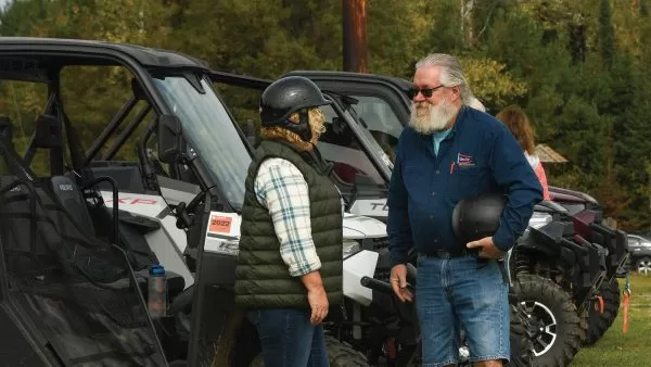 Two UTVers standing next to their parked vehicles talking while holding their helmets