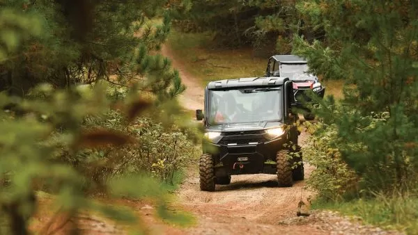 Two UTVs driving up a dirt path through the trees in summer